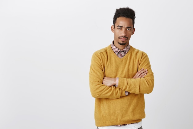 Doubt that your are telling me truth. suspicious serious african-american guy with afro hairstyle crossing hands and squinting, hesitating and looking with disbelief.