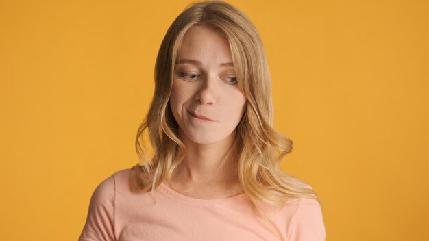 Doubtful blond girl thinking on camera over colorful background Thoughtful expression