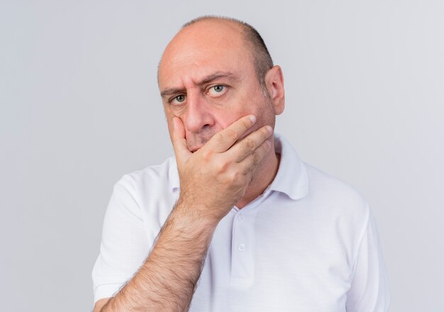 Doubtful casual mature businessman looking at camera keeping hand on mouth isolated on white background