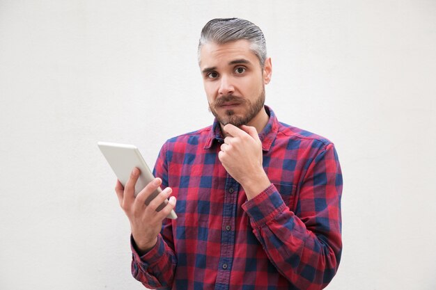 Doubtful man holding digital tablet