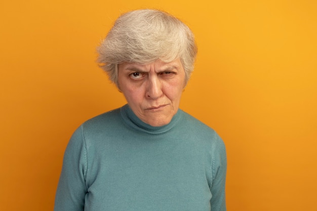 Foto gratuita dubbia vecchia donna che indossa un maglione blu a collo alto che guarda la parte anteriore isolata sulla parete arancione con spazio di copia