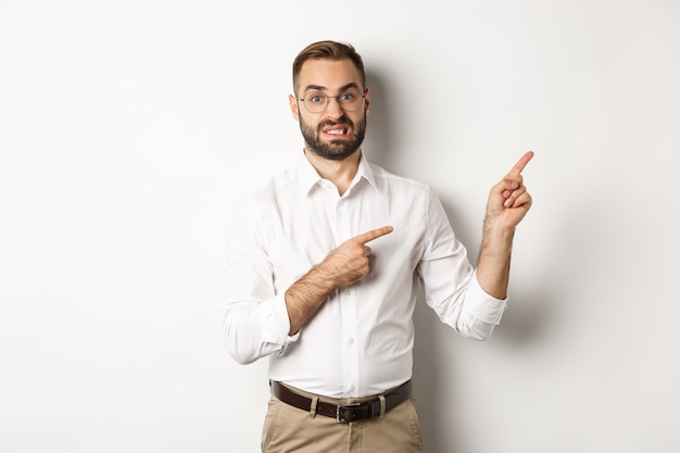 Doubtful and worried man looking indecisive, pointing at upper right corner hesitant, standing  