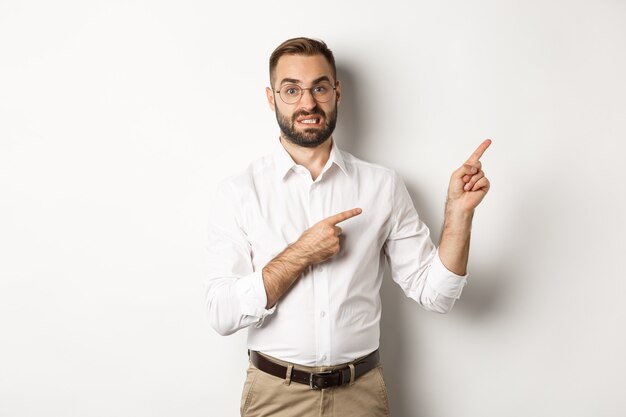 Doubtful and worried man looking indecisive, pointing at upper right corner hesitant, standing  