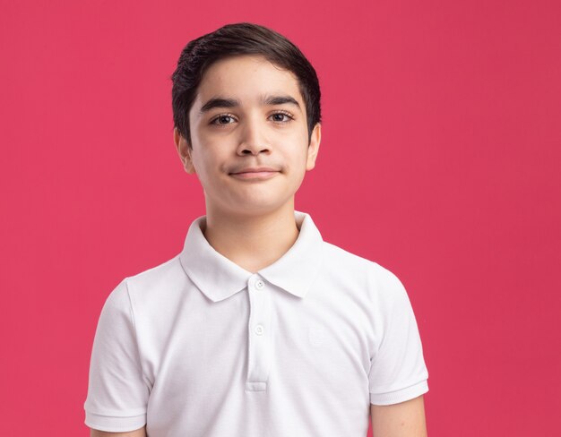 Doubtful young boy looking at front squinting eyes isolated on pink wall