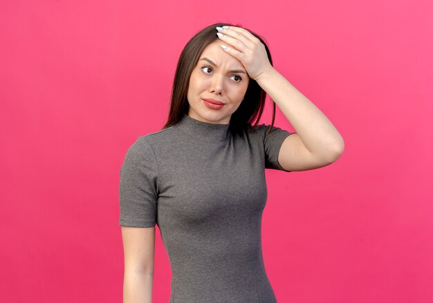 Doubtful young pretty woman looking straight putting hand on head isolated on pink background with copy space