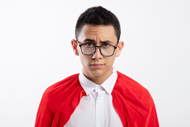 Free photo doubtful young superhero boy in red cape wearing glasses looking at camera isolated on white background