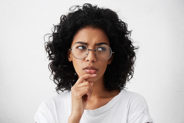 doubtful young woman wearing trendy round eyeglasses frowning