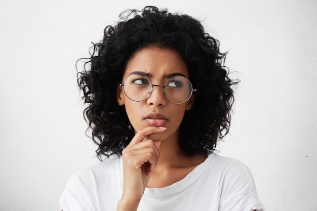 Free photo doubtful young woman wearing trendy round eyeglasses frowning