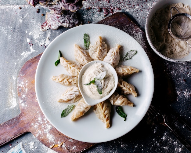 Dough dish a top view meat filled and with green leafs along with sour cream on the brown wooden surface