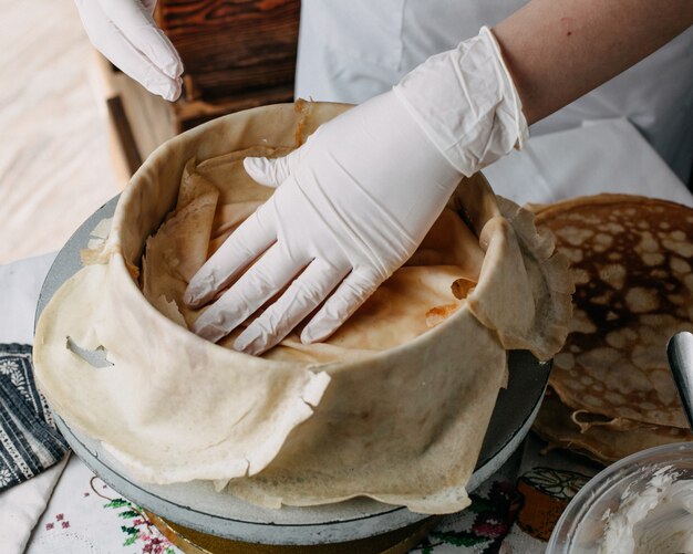 dough inside round pan with cook spreading slices on it inside kitchen