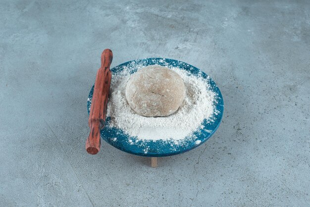 Dough roll with flour on wooden plate with rolling pin.