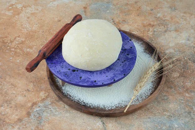 Dough with rolling pin and flour on marble table.