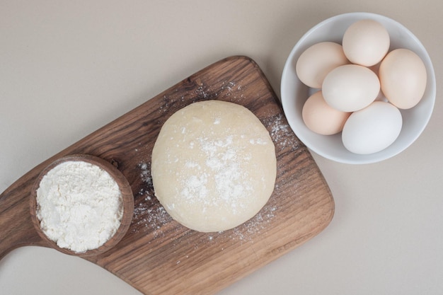Dough with three chicken fresh white eggs on wooden cutting board .