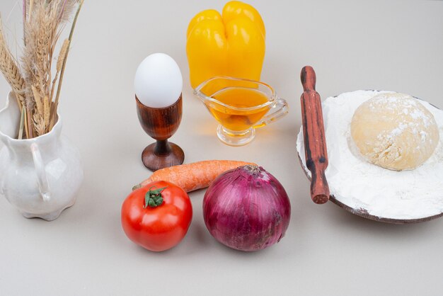 Dough with vegetables and egg on white surface