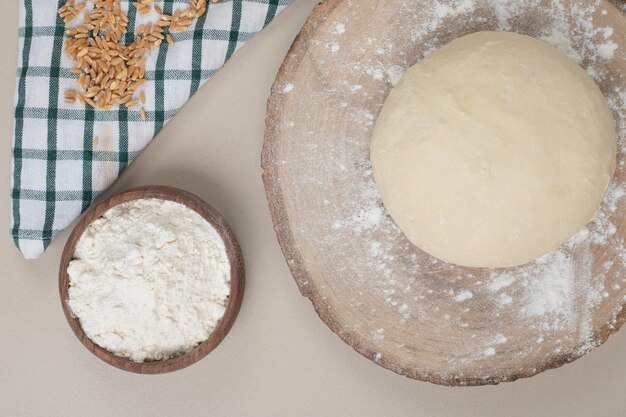 Dough with wooden bowl of flour on wooden board .