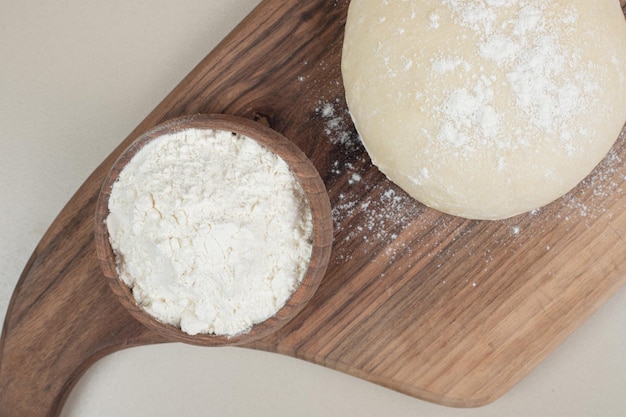 Dough with wooden bowl of flour on wooden cutting board .