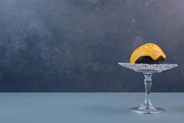 Doughnut on glass plate on marble table .