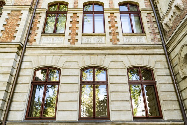 Down angle of arched windows on old beautiful building with sky and trees reflection in the glass