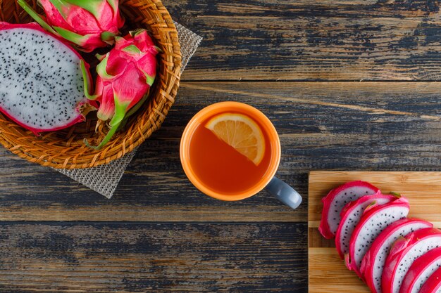 Dragon fruit in a basket with cutting board, tea flat lay on wooden table