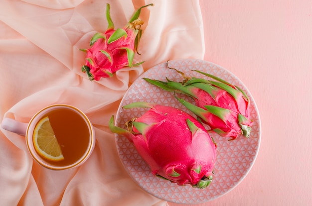 ピンクのテーブルに平らなお茶とプレートのドラゴンフルーツを置く
