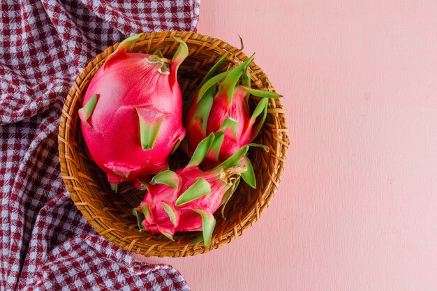 Dragon fruit in a wicker basket on pink and picnic cloth, flat lay.