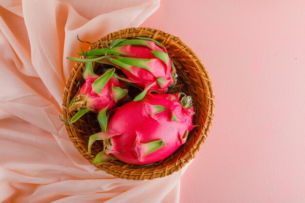 Dragon fruit in a wicker basket on pink table. flat lay.