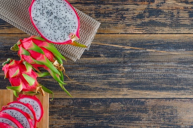 Dragon fruit with cutting board on wooden table, top view.