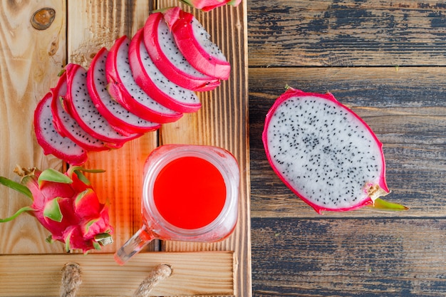 Free photo dragon fruit with juice in a tray on wooden table, flat lay.