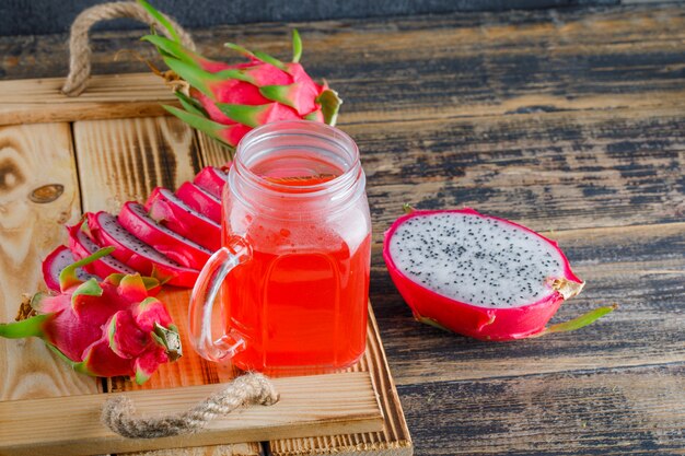 Dragon fruit with juice in a tray on wooden table, high angle view.