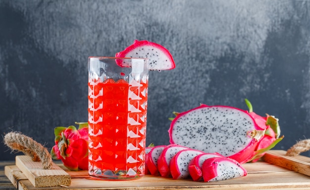 Dragon fruit with juice in a tray on wooden table and plaster wall, side view.