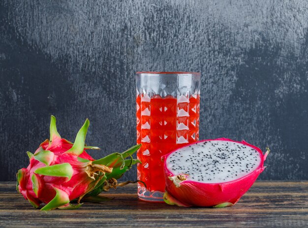 Dragon fruit with juice on wooden table and plaster wall, side view.