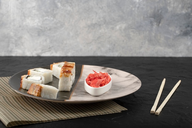 Суши-роллы дракон с угрем и маринованным имбирем на мраморной тарелке