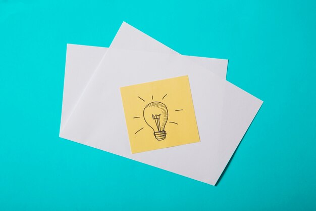 Drawn light bulb on yellow sticky note over the turquoise background