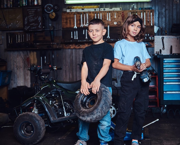 드림팀이 활동 중 - 두 아이가 자동차 워크숍에서 사진사를 위해 포즈를 취하면서 즐거운 시간을 보내고 있습니다.