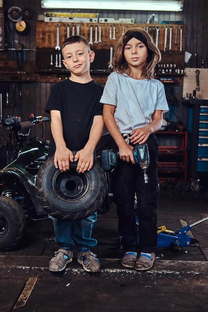 Foto gratuita dream team in azione: due bambini si divertono mentre posano per il fotografo in un'officina automobilistica.