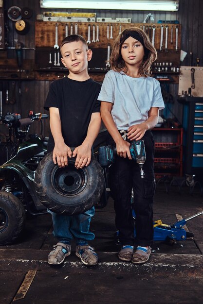 드림팀이 활동 중 - 두 아이가 자동차 워크숍에서 사진사를 위해 포즈를 취하면서 즐거운 시간을 보내고 있습니다.