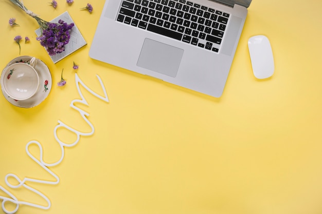 Dream word near laptop and empty cup on yellow surface