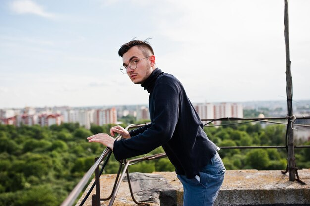 Free photo dreamer stylish macho man in black golf and glasses posed on the roof