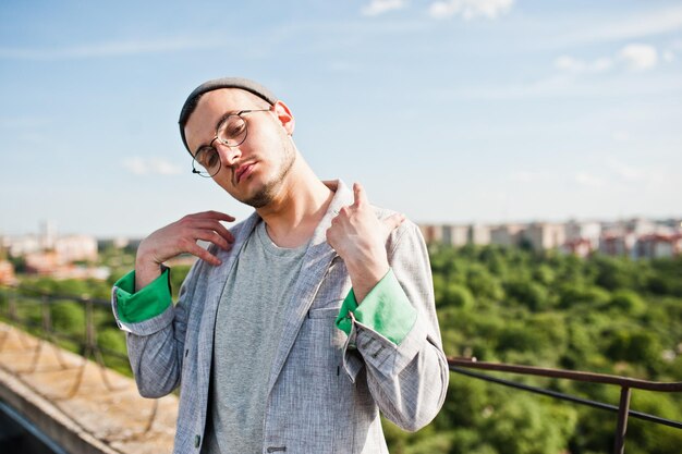 Dreamer stylish macho man in gray suit hat and glasses posed on the roof