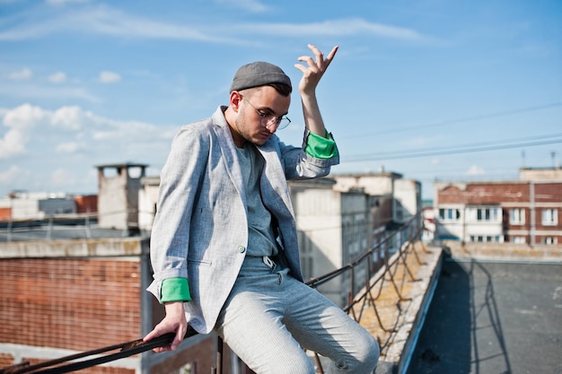 Free photo dreamer stylish macho man in gray suit hat and glasses posed on the roof