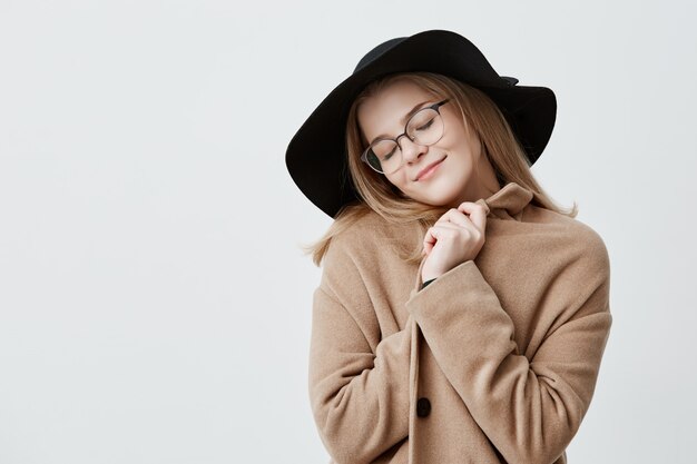 Dreamful positive female in retro outfit, wraps in coat, stands  with closed eyes, imagines something pleasant, tries to relax. Positive human emotions and feelings concept