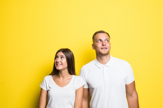 Dreaming young couple isolated on yellow background together dressed up in white t-shirts