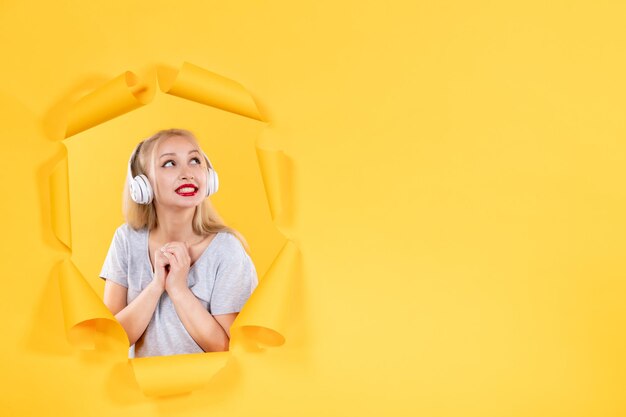 Dreaming young female in headphones on torn yellow paper background sound ultrasound music audio