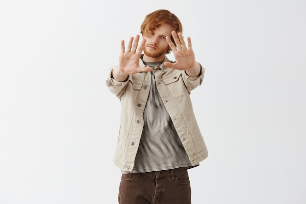 Dreamy bearded redhead guy posing against the white wall