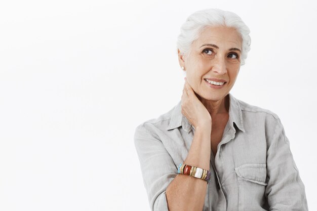 Dreamy beautiful old lady, touching neck and looking upper left corner thoughtful