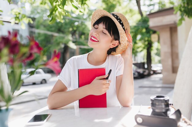 Dreamy brunette girl in straw hat with black ribbon thinking about something pleasant with eyes closed