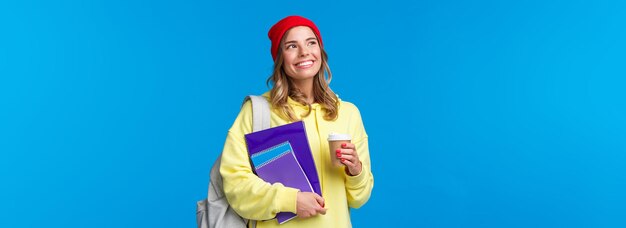 Una studentessa universitaria carina e sognante che contempla la soleggiata giornata primaverile mentre si reca alle lezioni che tengono caffè da asporto