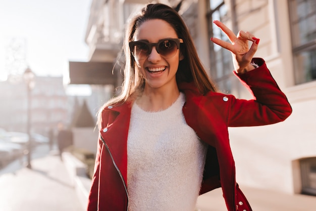 Dreamy girl wears white shirt and red jacket expressing happiness on the street