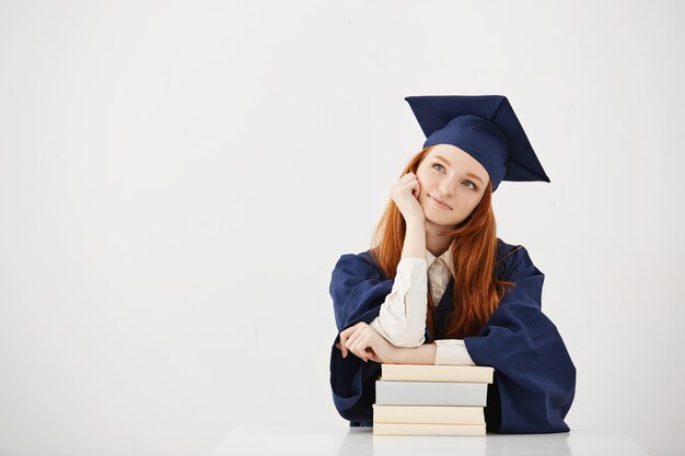 Мечтательный выпускник женщина улыбается мышления сидя с книгами.