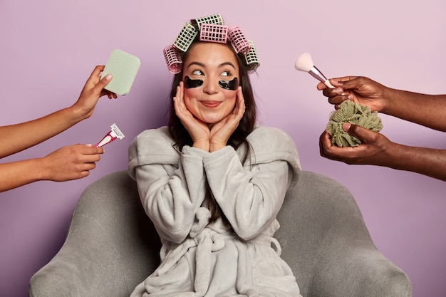 Dreamy happy woman poses with eyes patches and curlers